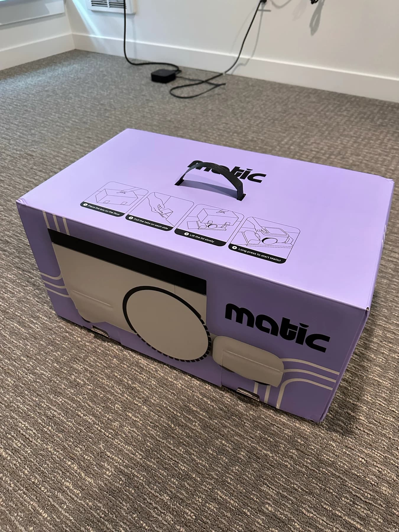 The top and front of Matic's purple box, with a black carry handle and illustrated unpacking instructions